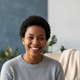 Smiling person's headshot, conveying trust and happiness, with a soft background in slate blue, bright white, and warm cream.